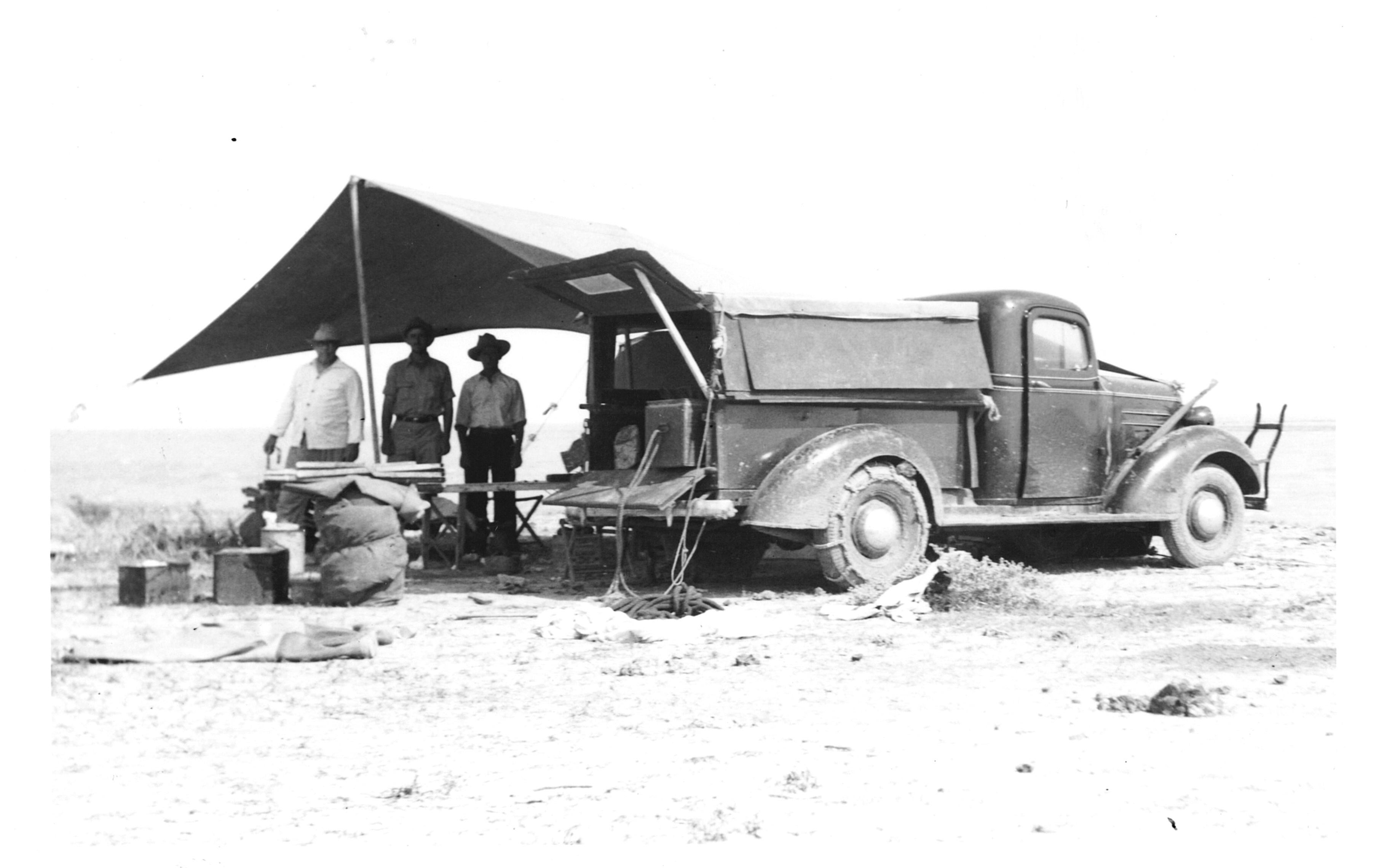 Three men stand next to a truck in the 1900s